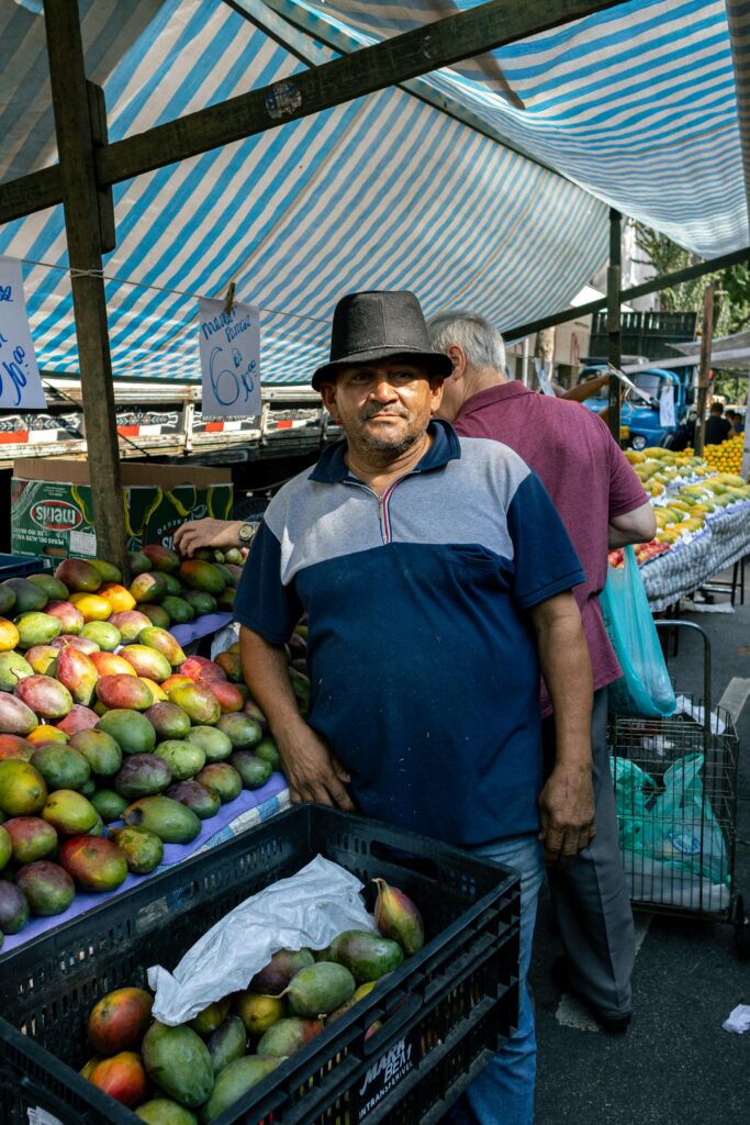 A vendor stands proudly with his fresh mangoes at a bustling São Paulo market.